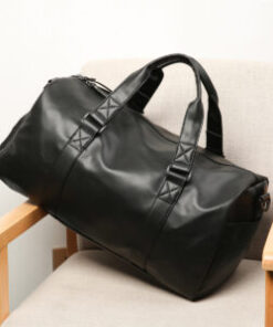 A black leather Chaomen's Fitness Bag with two handles and zipper closure rests on a beige chair with wooden armrests.