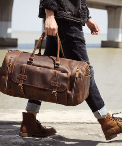 A person holding a stylish brown leather luggage bag with multiple zippers and buckles.